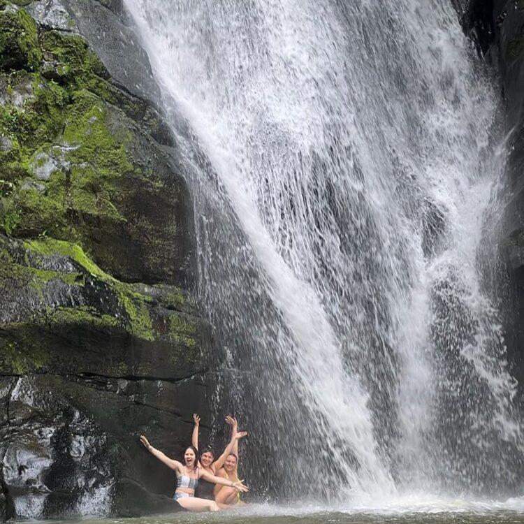 Three women sit next to a massive waterfall in Costa Rica