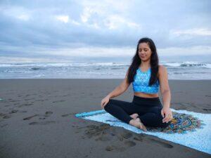 Women sits on a yoga mat and meditate on beach