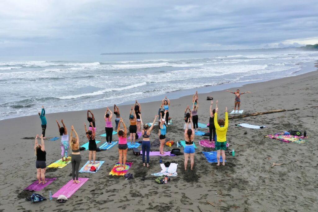 A large group practice yoga on a beach, ocean in background