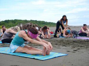 A woman does yoga on the beach and reaches for her toes